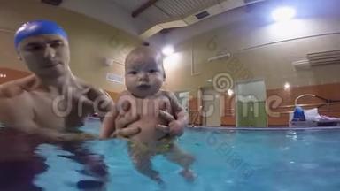 带着孩子在游泳池里的年轻父亲。在游泳池里游泳。对婴儿进行的复杂的锻炼。